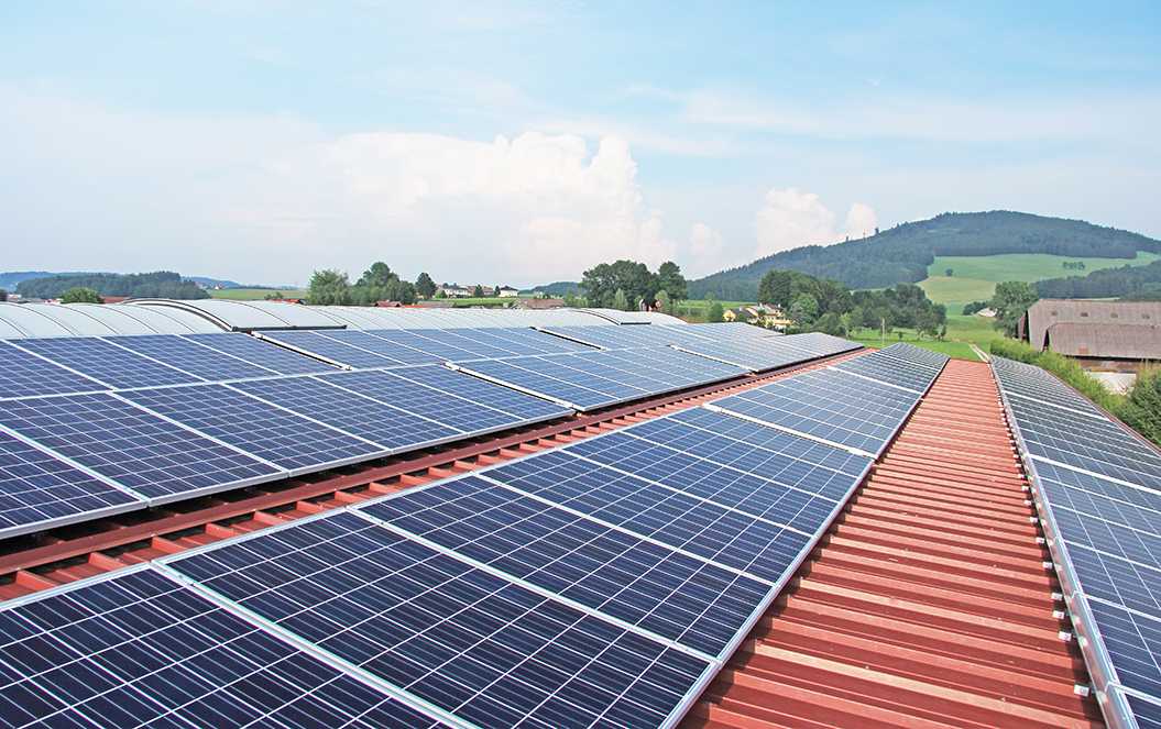 Photovoltaikanlage welche durch eine Photovoltaikversicherung gesichert ist, auf einem Hausdach bei strahlendem Sonnenschein. Die Solarmodule sind zur Sonne hin ausgerichtet, um maximale Energieeffizienz zu gewährleisten. Im Hintergrund blauer Himmel und grüne Bäume, die die umweltfreundliche Energiegewinnung durch Solarenergie symbolisieren.