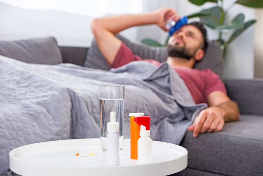 Ein kranker Mann liegt mit Medikamenten auf dem Sofa – eine Reiseabbruchversicherung schützt vor finanziellen Verlusten bei Krankheit.