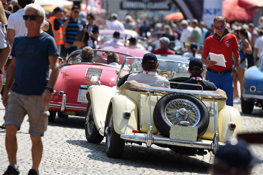 Rückansicht mehrerer Oldtimer bei einer Rallye mit zahlreichen Zuschauern und Teilnehmern.