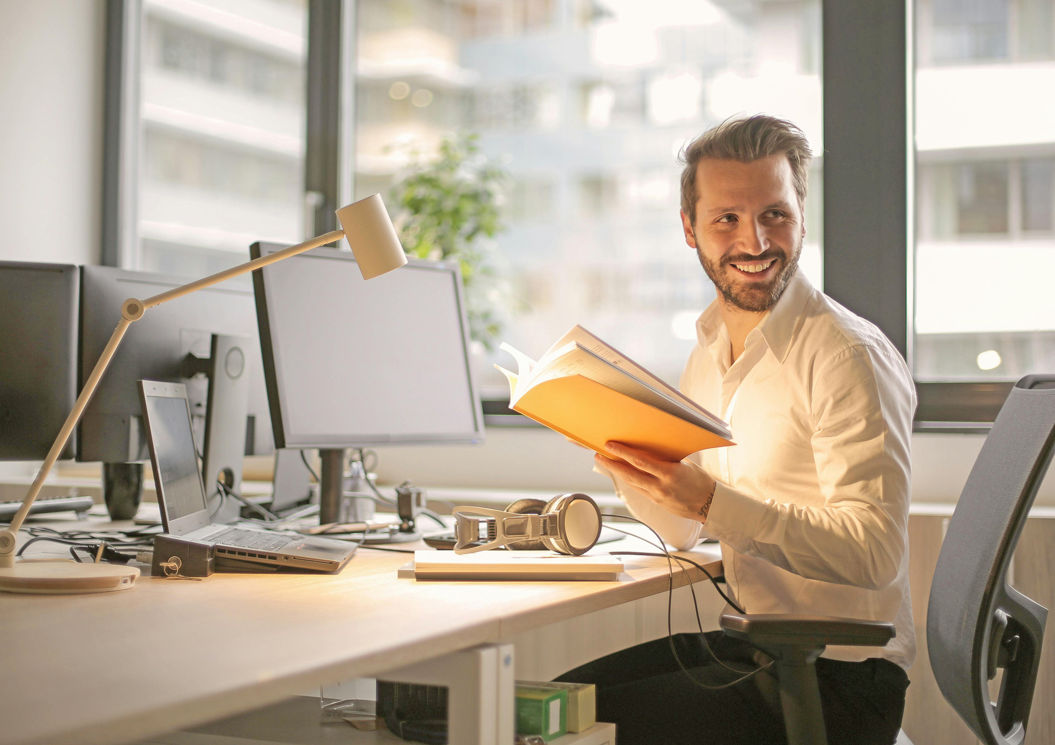 Lächelnder Mann sitzt im modernen Büro mit geöffnetem Ordner in der Hand – Symbolbild dafür, eine private Krankenzusatzversicherung in Leipzig abzuschließen.