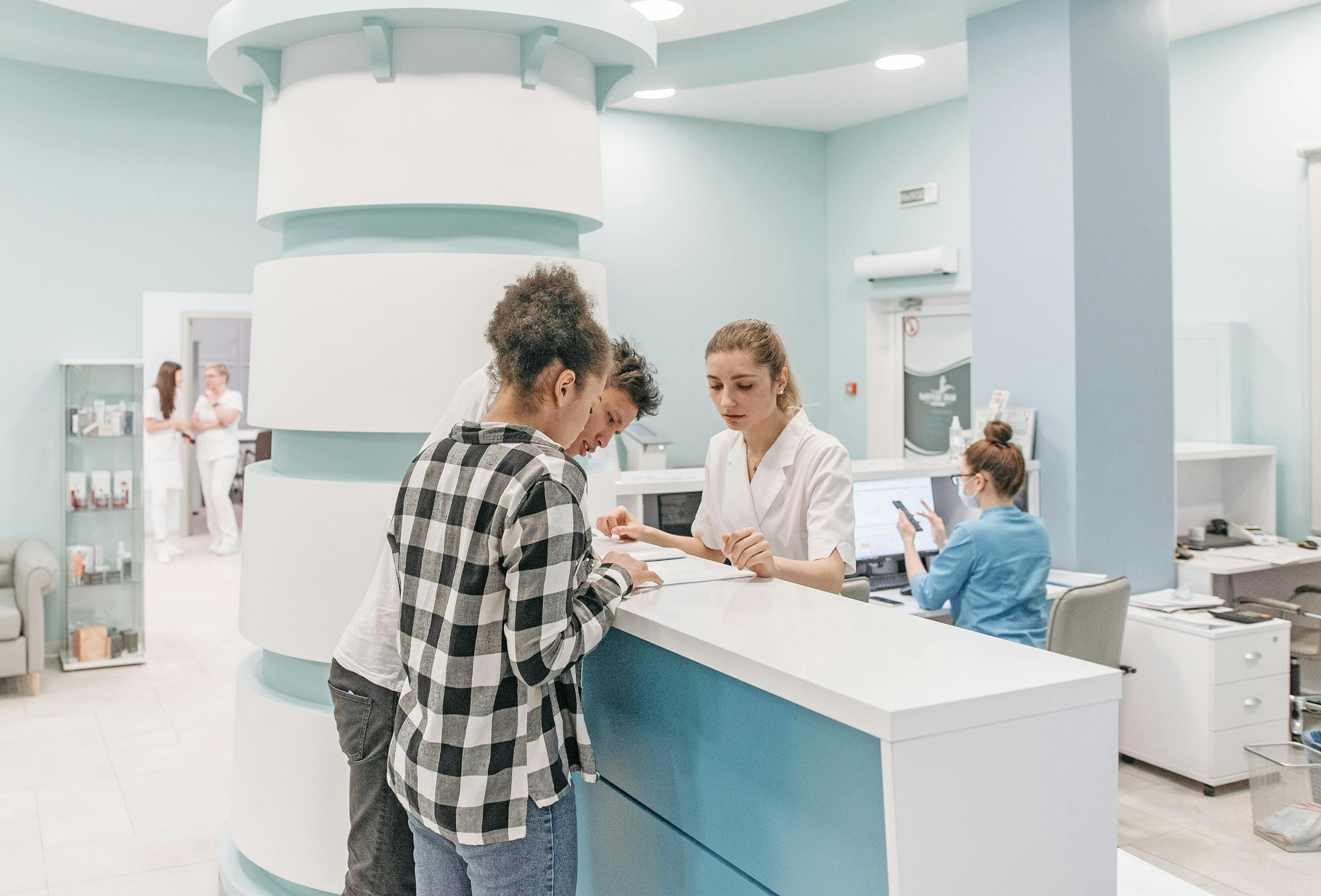 Junges Paar lässt sich am Empfang einer modernen Arztpraxis von einer Mitarbeiterin zu Unterlagen beraten – Symbolbild für Private Krankenzusatzversicherung in Leipzig.