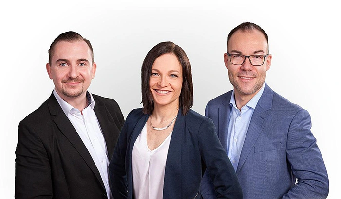 Drei sympathische und professionell gekleidete Personen stehen nebeneinander. Die Gruppe besteht aus André Brumme, Claudia Liebmann und Marcus Aßmann. Das Bild repräsentiert unabhängige Finanzberater und Versicherungsmakler aus Leipzig, die kompetente Beratung und maßgeschneiderte Versicherungslösungen anbieten.