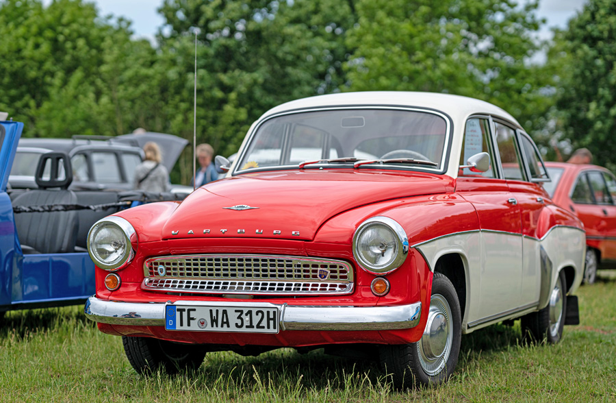 Rote-weißer Wartburg-Oldtimer steht auf einer Wiese bei einer Oldtimer-Ausstellung.