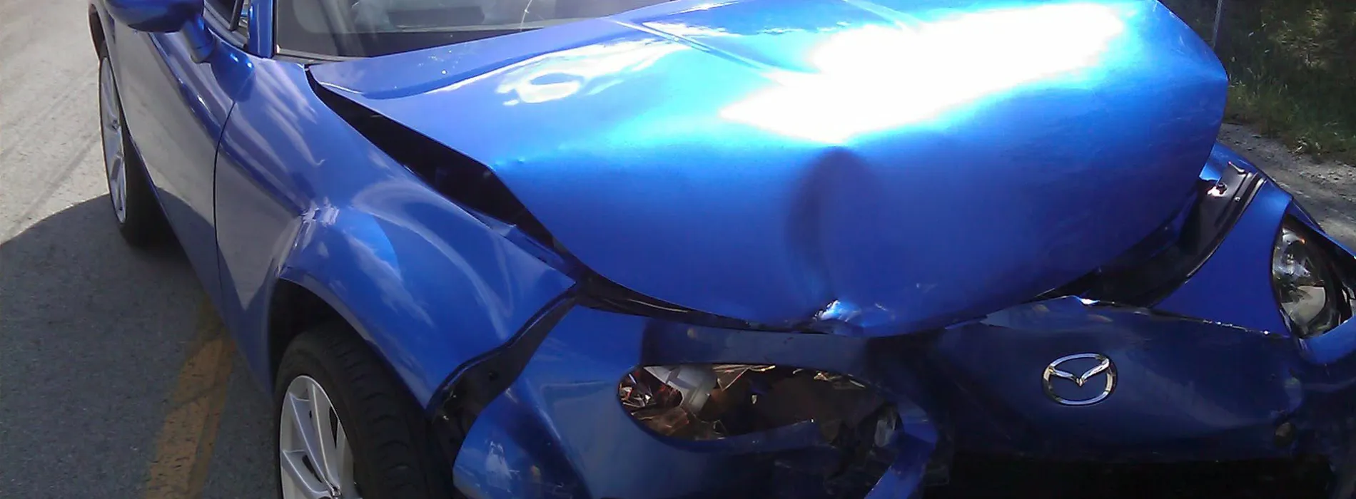  Blauer Mazda mit starkem Frontschaden nach einem Unfall – Symbolbild für günstige Autoversicherung in Leipzig.