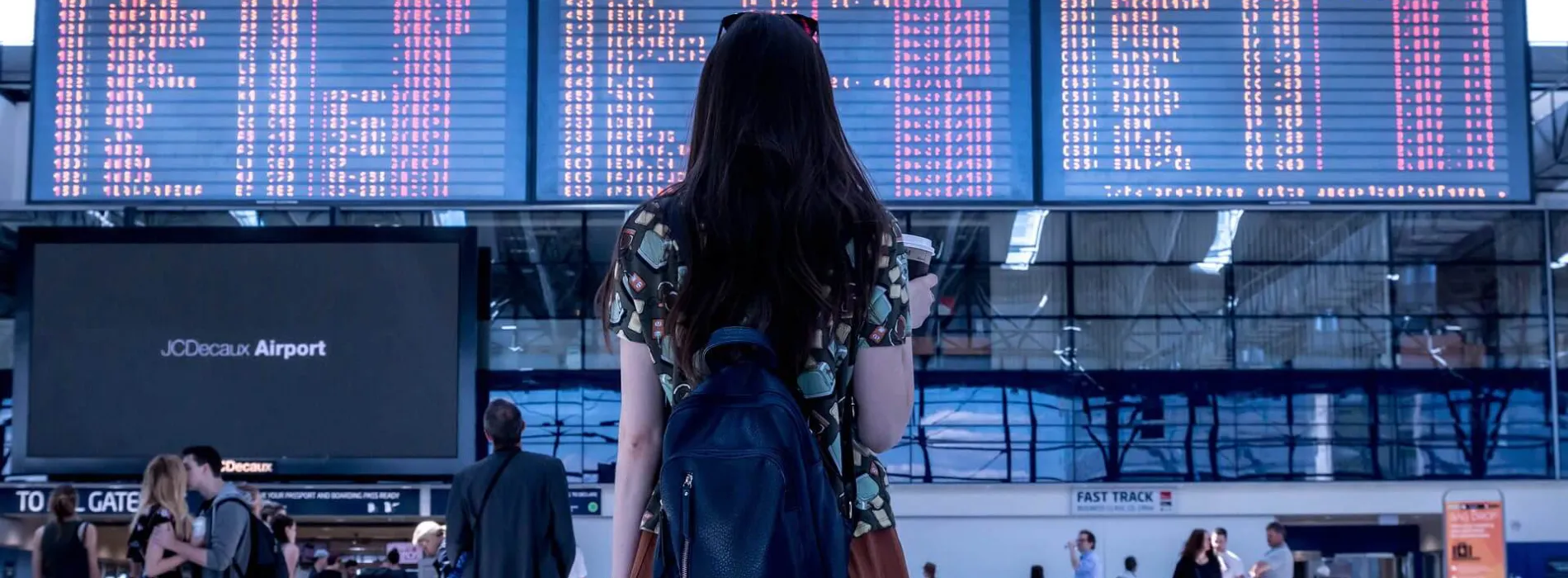  Frau mit Rucksack blickt auf die Abflugtafel am Flughafen – Symbolbild für Reiserücktrittsversicherung in Leipzig.