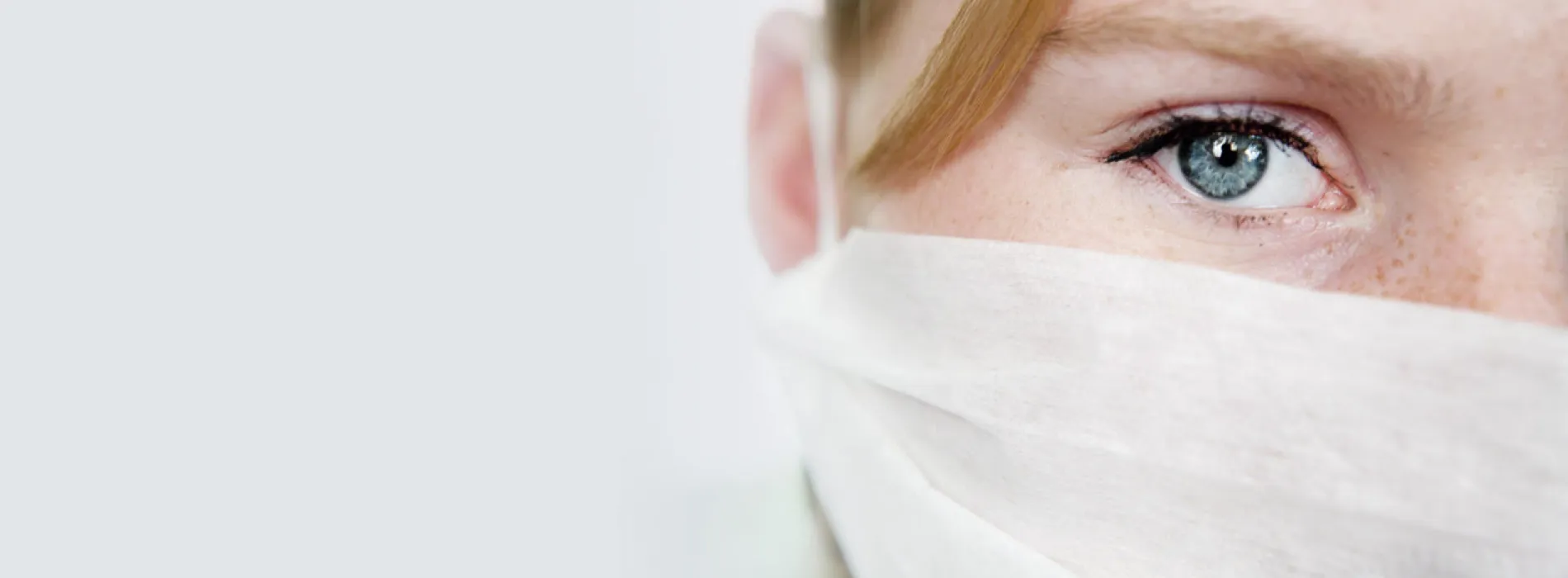  Nahaufnahme eines besorgten Gesichts mit Mundschutz – symbolisch für den Schutz durch eine schwere Krankheiten Versicherung in Leipzig.
