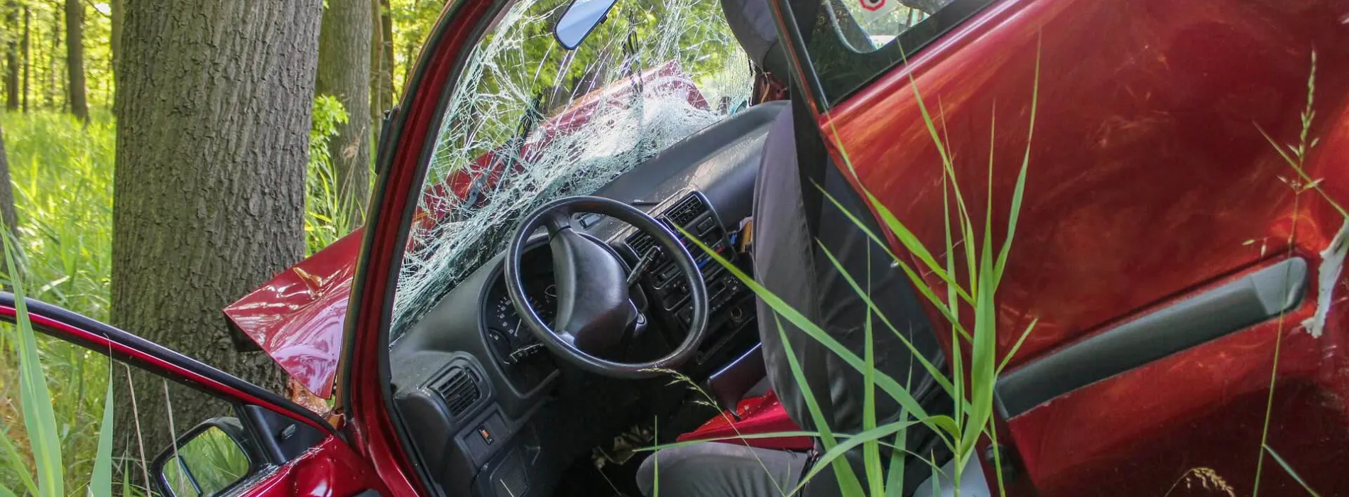  Rotes Auto mit starkem Unfallschaden gegen Baum im Wald – Symbolbild für die Notwendigkeit einer privaten Unfallversicherung in Leipzig.