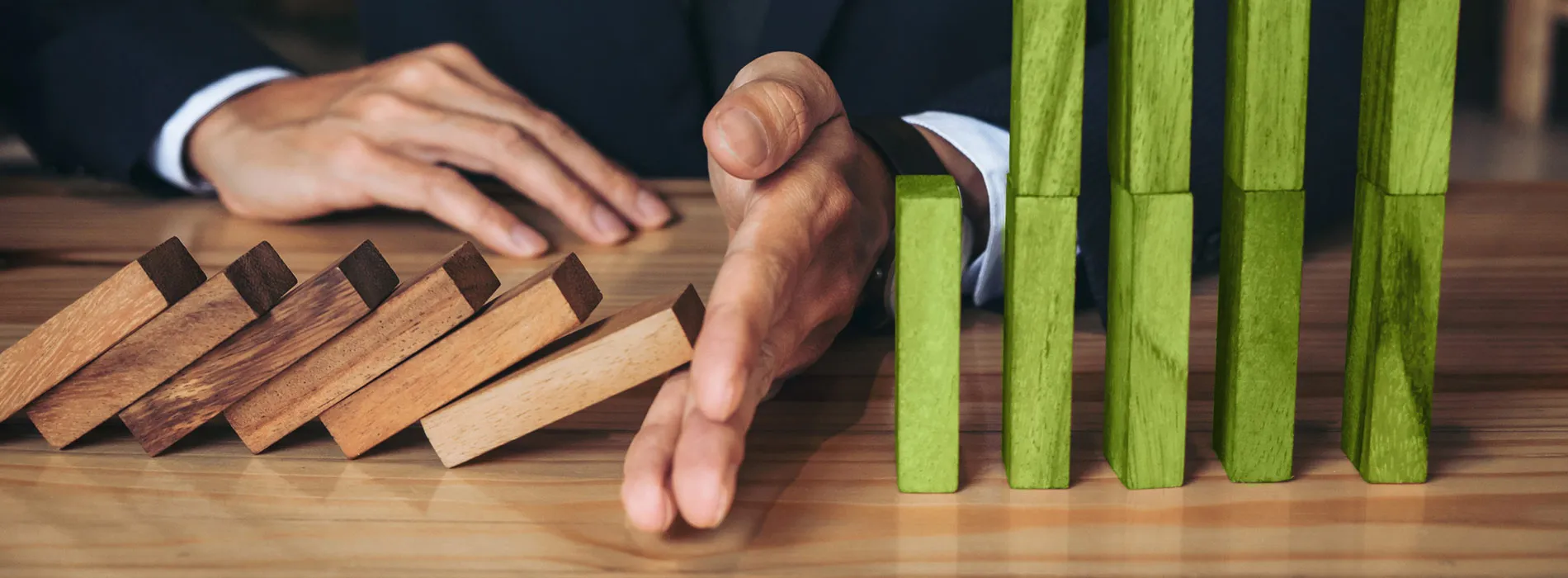Eine Hand stoppt fallende Holzklötze, grüne Blöcke stehen stabil – symbolisiert den Schutz durch Versicherungen für Unternehmen in Leipzig.