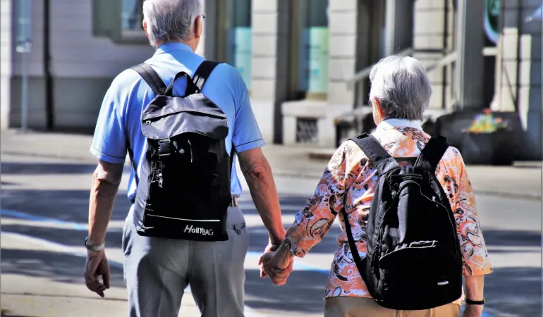 Älteres Paar mit Rucksäcken Hand in Hand in der Stadt unterwegs – Symbolbild für Altersvorsorge und finanziell abgesichertes Alterseinkommen