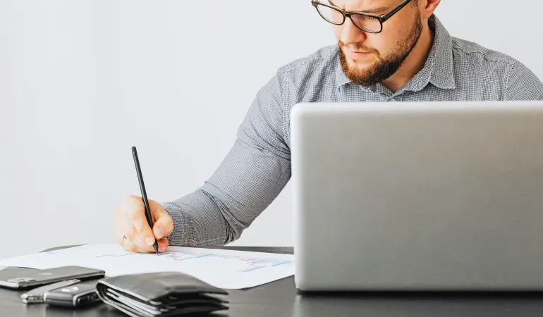 Mann arbeitet konzentriert am Laptop und berechnet Zahlen auf einem Blatt – Symbolbild für die neuen Beitragsbemessungsgrenzen 2026.
