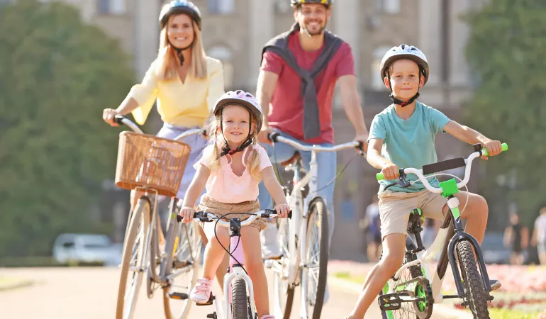 Fröhliche Familie beim gemeinsamen Radfahren im Park. Zwei Erwachsene und zwei Kinder tragen Helme und fahren auf modernen Fahrrädern. Das Bild symbolisiert die Bedeutung von umweltfreundlicher Mobilität im Alltag und hebt hervor, dass eine Fahrradversicherung zusätzlichen Schutz und Sicherheit bietet.