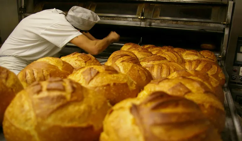  Bäcker bei der Arbeit in einer Backstube mit frisch gebackenem Brot – Symbolbild für maßgeschneiderte Gewerbeversicherungen in Leipzig.