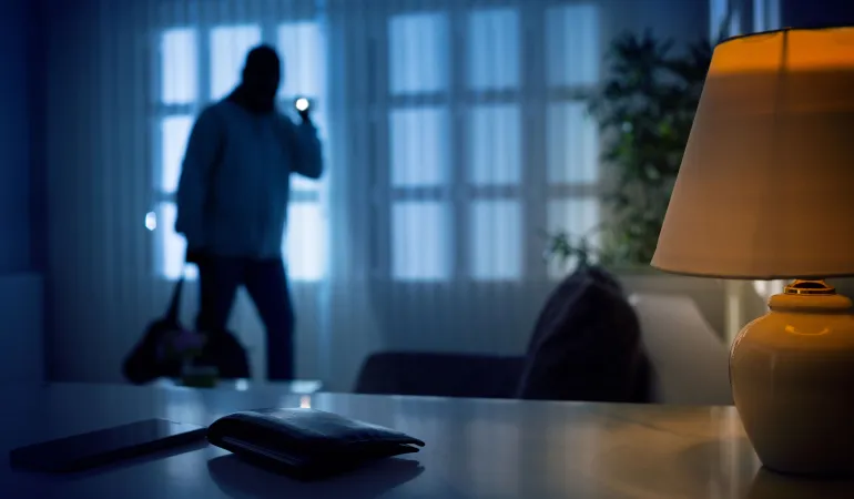 Ein Einbrecher dringt nachts in ein Wohnzimmer ein – ein starker Einbruchsschutz über die Immobilienversicherung schützt in Leipzig vor hohen Schäden.