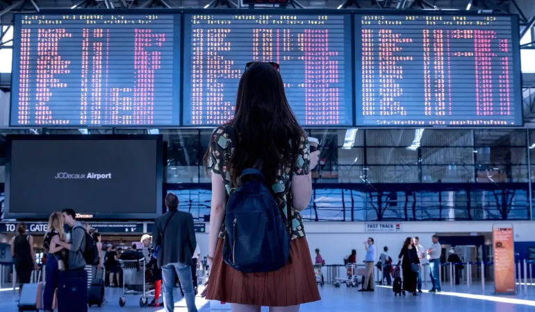 Frau mit Rucksack blickt auf die Abflugtafel am Flughafen – Symbolbild für Reiserücktrittsversicherung in Leipzig.
