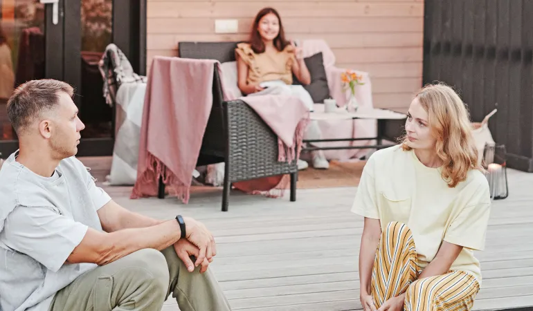Drei Menschen verbringen gemeinsam einen entspannten Nachmittag auf der Terrasse eines Holzhauses