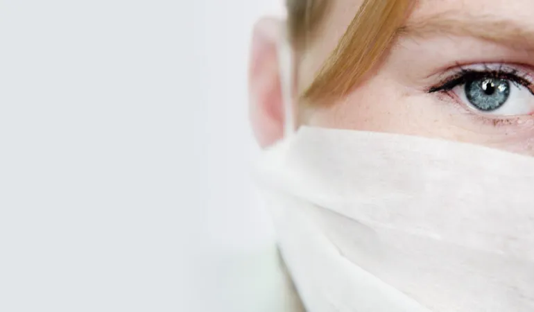  Nahaufnahme eines besorgten Gesichts mit Mundschutz – symbolisch für den Schutz durch eine schwere Krankheiten Versicherung in Leipzig.