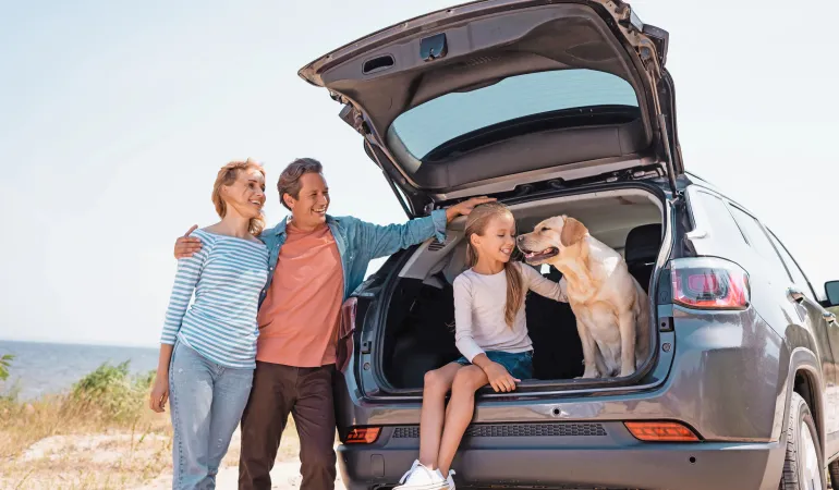 Familie mit Kind und Hund genießt den Urlaub am Meer – das Auto ist durch eine Vollkaskoversicherung abgesichert